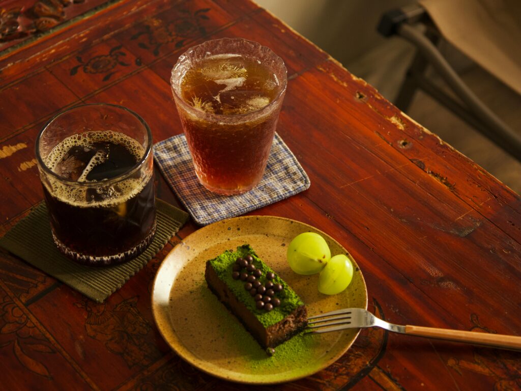 Two iced coffee drinks with a green tea cake and grapes on a rustic table setting.
